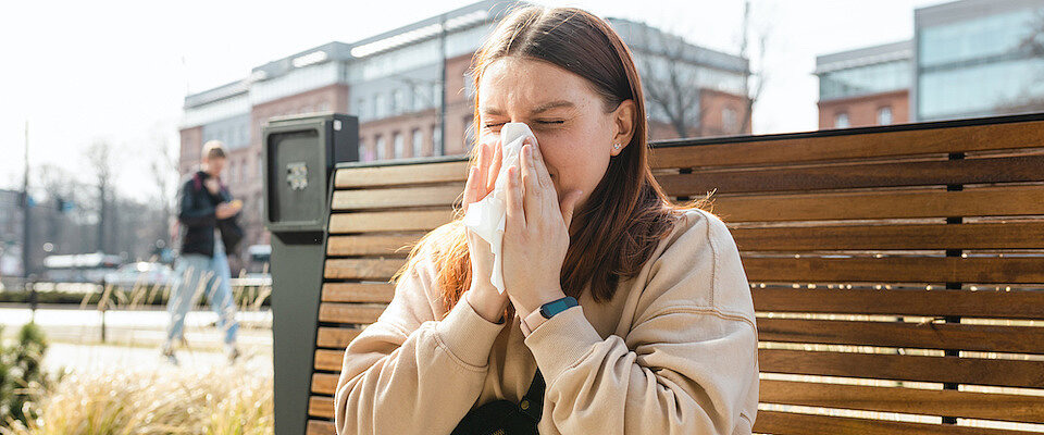 Eine Frau sitzt auf einer Bank und putzt sich die Nase