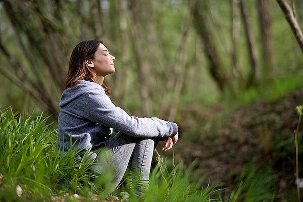 Eine Frau sitzt mit geschlossenen Augen im Wald auf dem Boden
