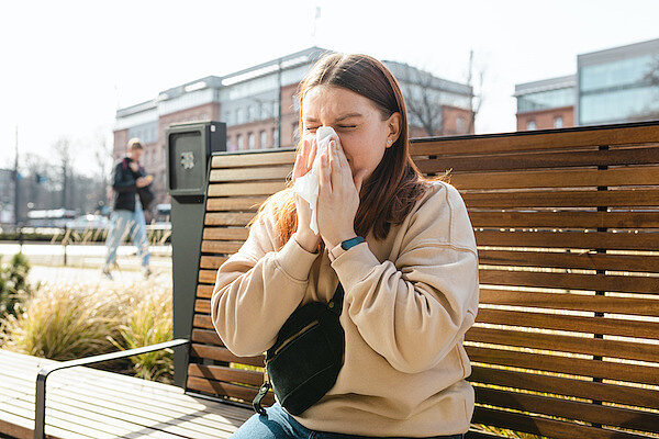 Eine Frau sitzt auf einer Bank und putzt sich die Nase
