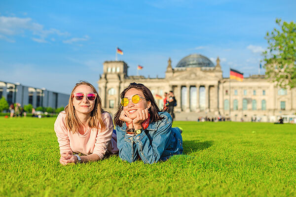 Zwei Mädchen liegen auf einer Wiese in Berlin vor dem Reichstag