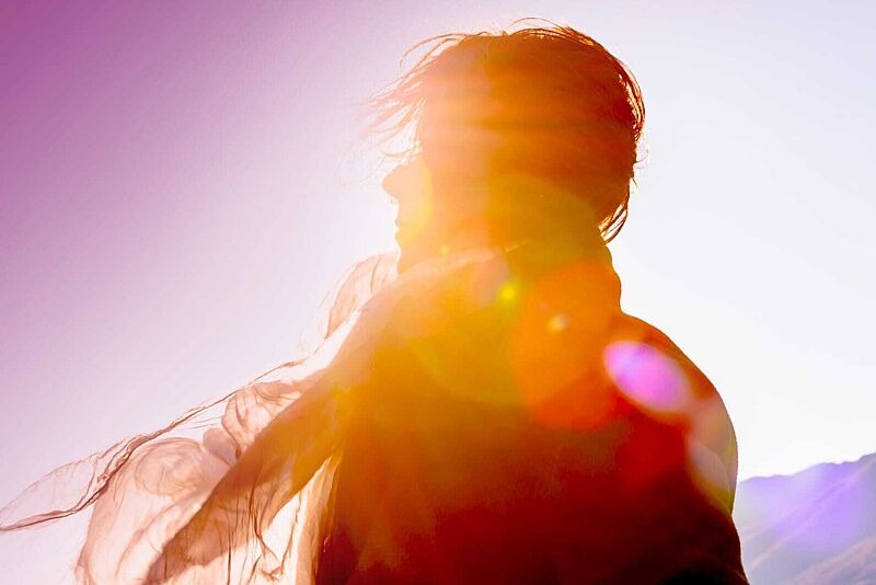 Eine Person mit flatterndem Schal steht im Gegenlicht der Sonne