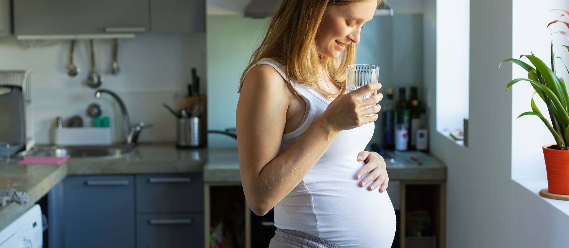 Schwangere Frau steht mit einem Glas wasser in der Küche