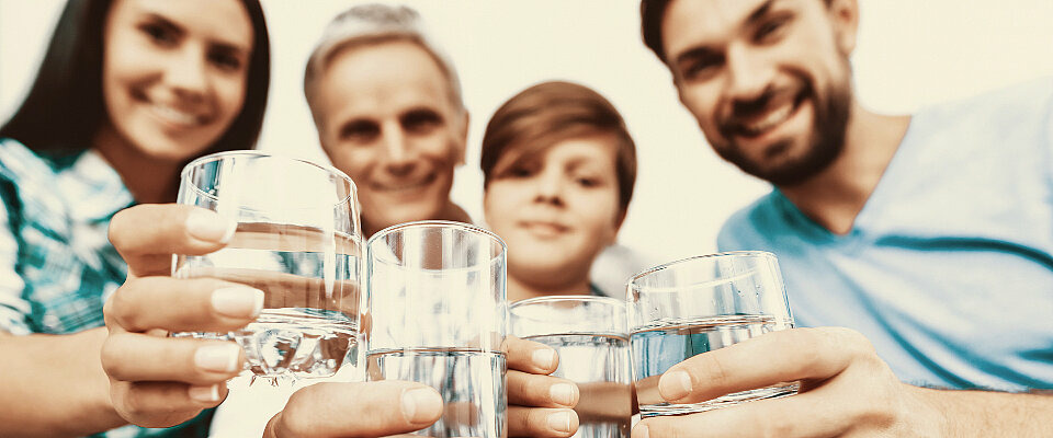 Eine fröhliche Familie hält Gläser mit Wasser vor sich. 