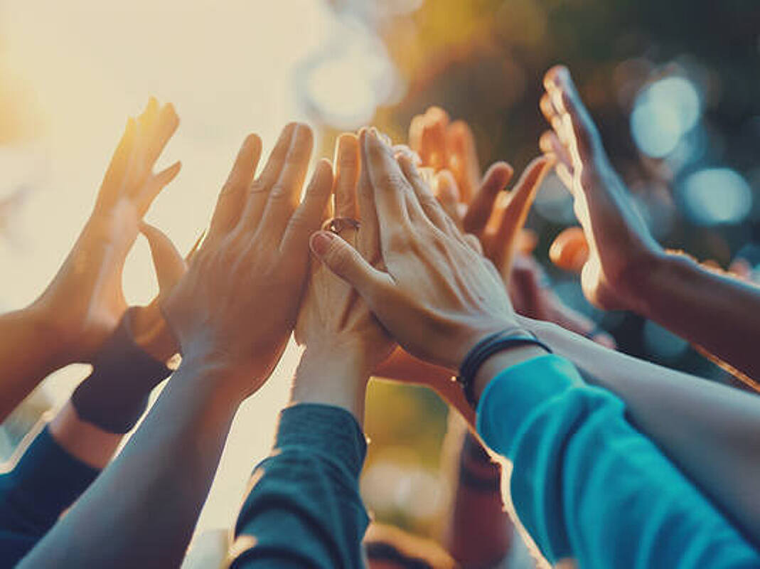 Mehrere Hände werden im Kreis in die Luft gestreckt und berühren sich dabei