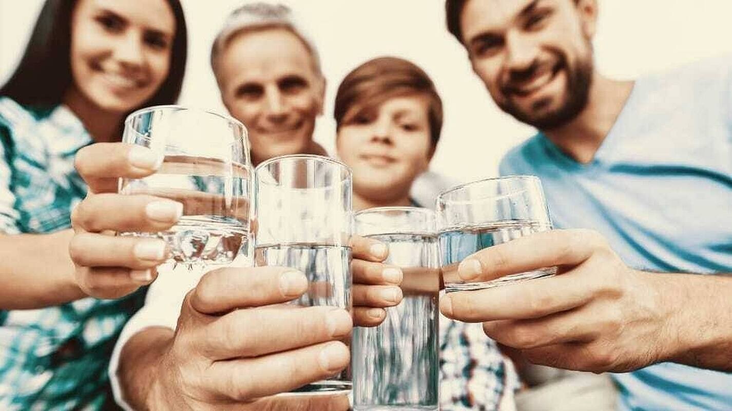 Eine fröhliche Familie hält Gläser mit Wasser vor sich. 