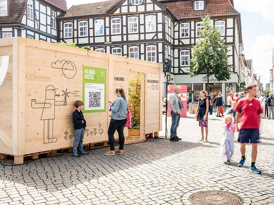Mehrere Menschen stehen in der Innenstand vor einer Klima-Kiste.