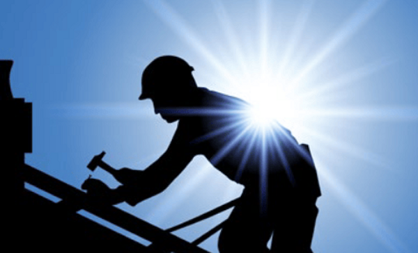 Ein Dachdecker bei der Arbeit im Gegenlicht vor blauem Himmel