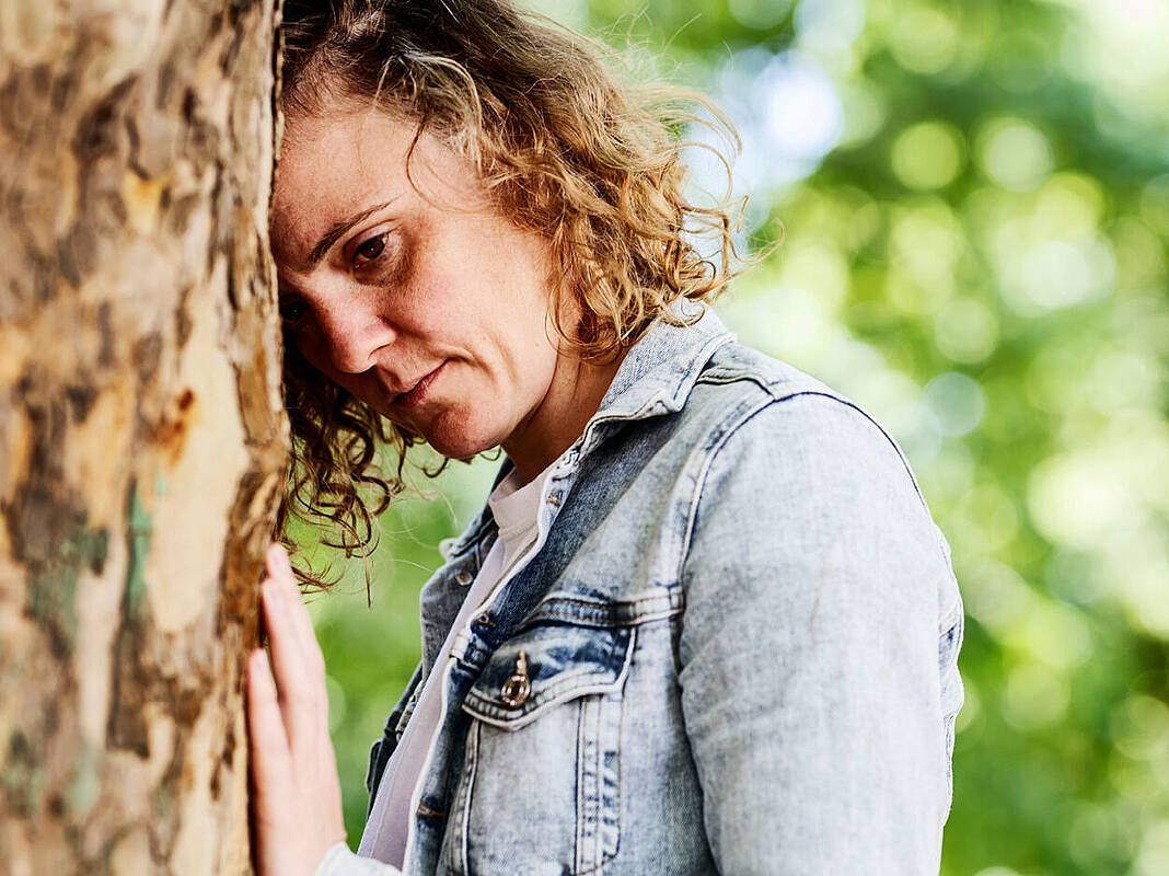 Eine Frau lehnt sich bedrückt an einen Baumstamm.